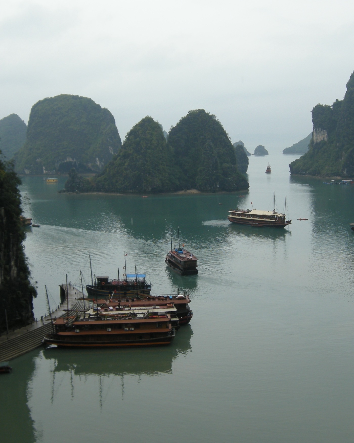 Perahu kayu tradisional di antara pulau batu kapur di Teluk Ha Long