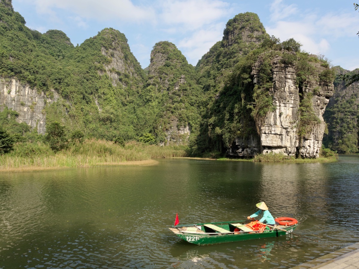 Perahu kecil di sungai di bawah tebing batu kapur di Trang An